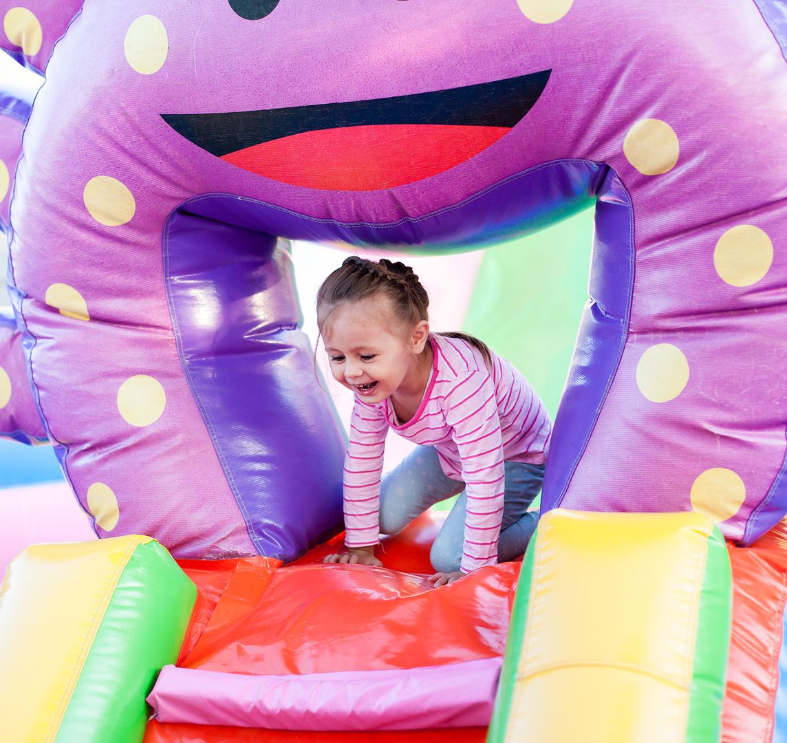 Ein Mädchen springt vergnügt auf einer bunten, aufblasbaren Hüpfburg und hat sichtlich Spaß beim Spielen.