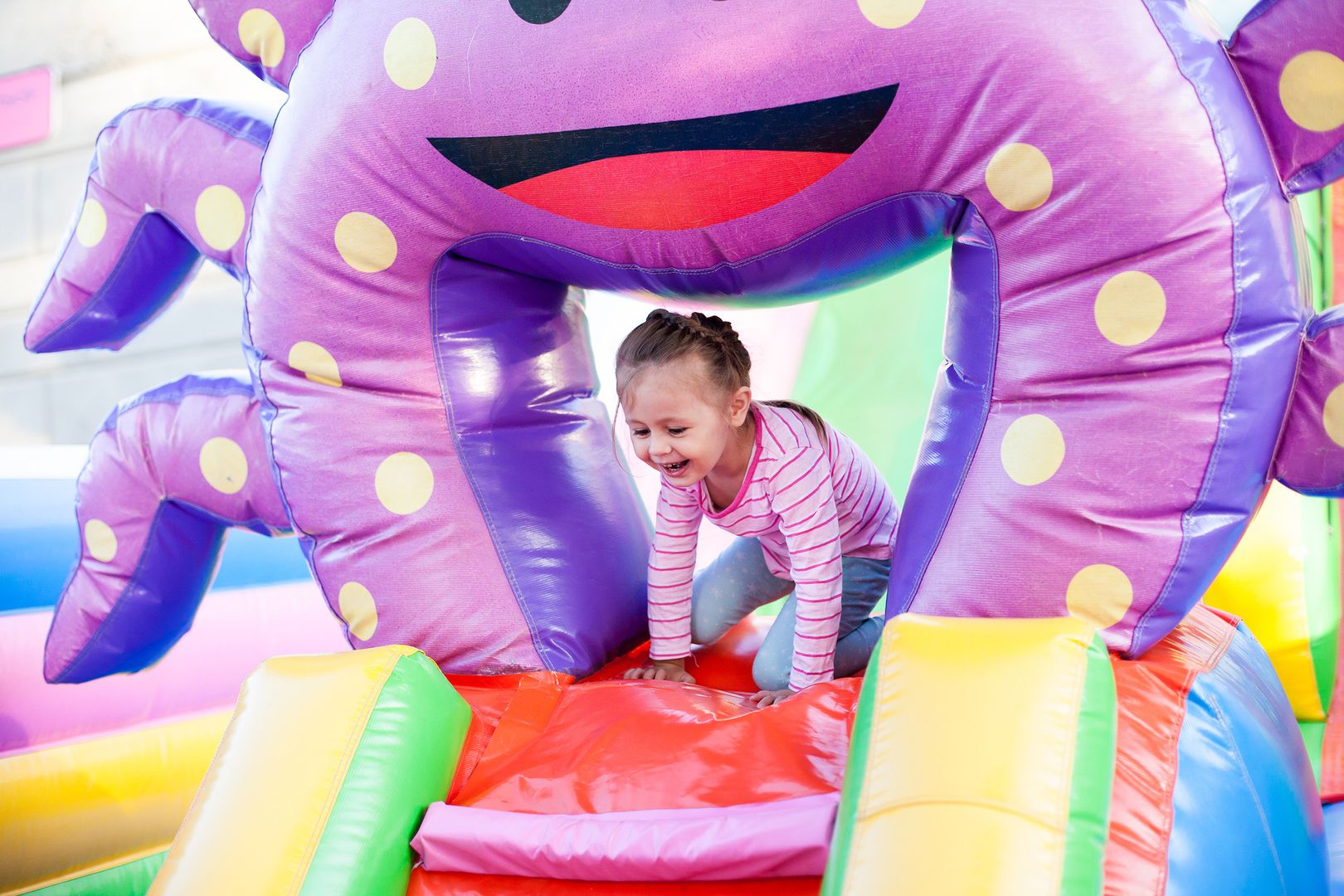Ein Mädchen erklimmt einen bunten, aufblasbaren Krebs und hat sichtlich Spaß beim Spielen im Freien.